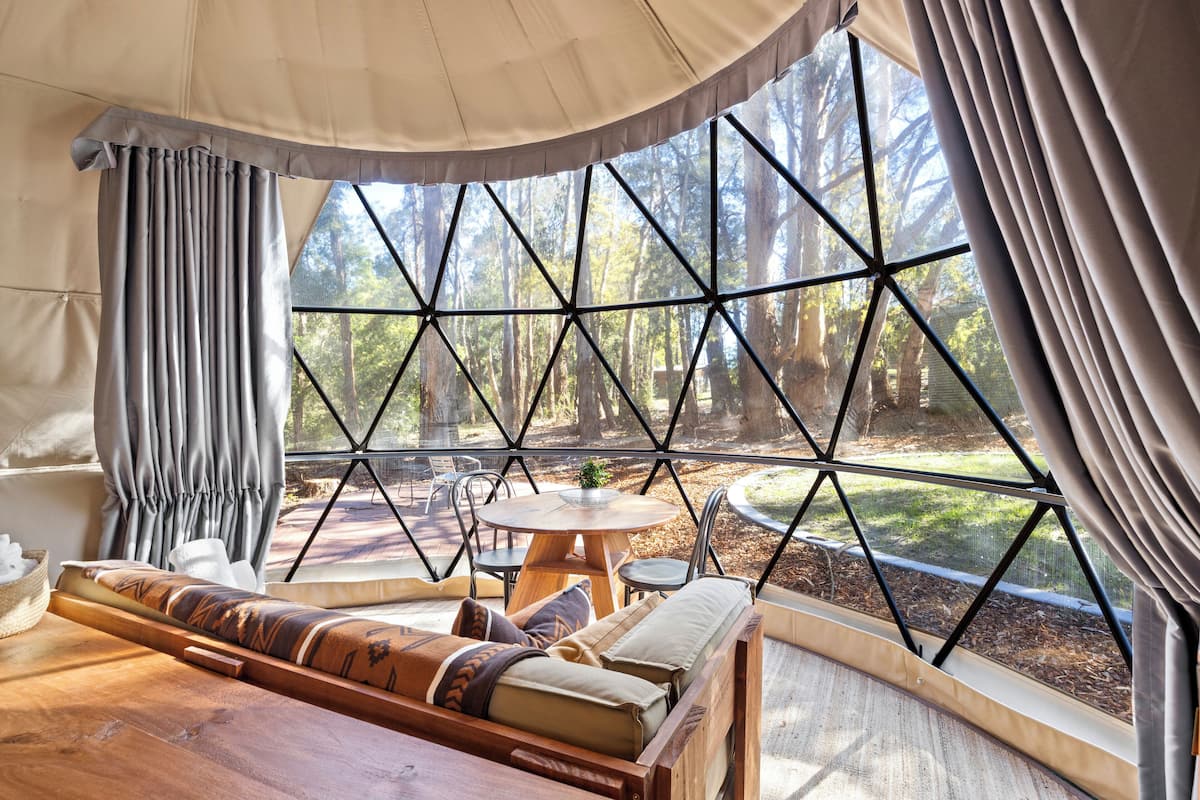 A cozy tented room with a large window, a wooden table, and a cushioned seating area.