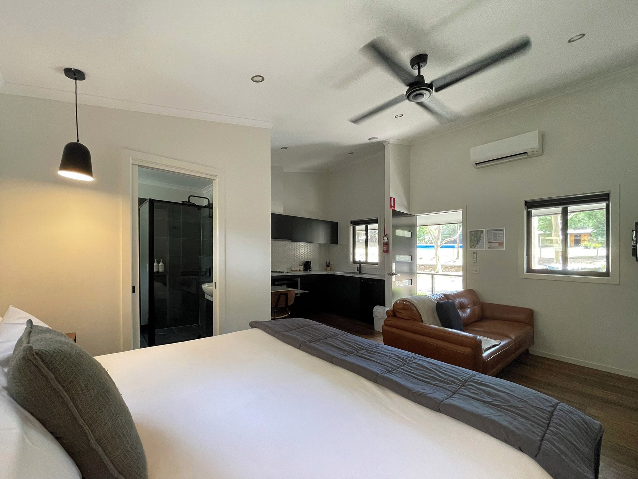 Une chambre à coucher avec un lit, un ventilateur de plafond, une fenêtre et une vue sur la cuisine.