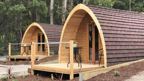 Dos cabañas de madera con puertas arqueadas, cada una con un pequeño balcón con mesa y sillas.