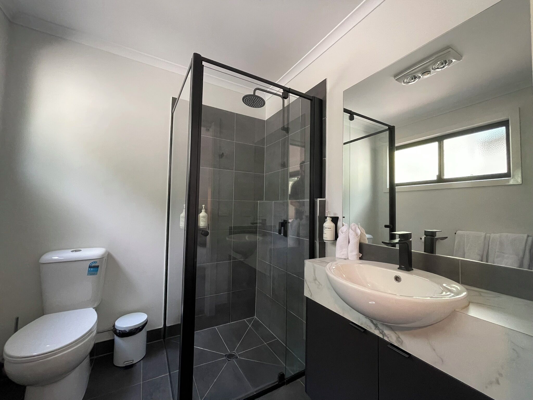 A modern bathroom with a glass-enclosed shower, a white toilet, a sink with a marble countertop, and a large mirror.