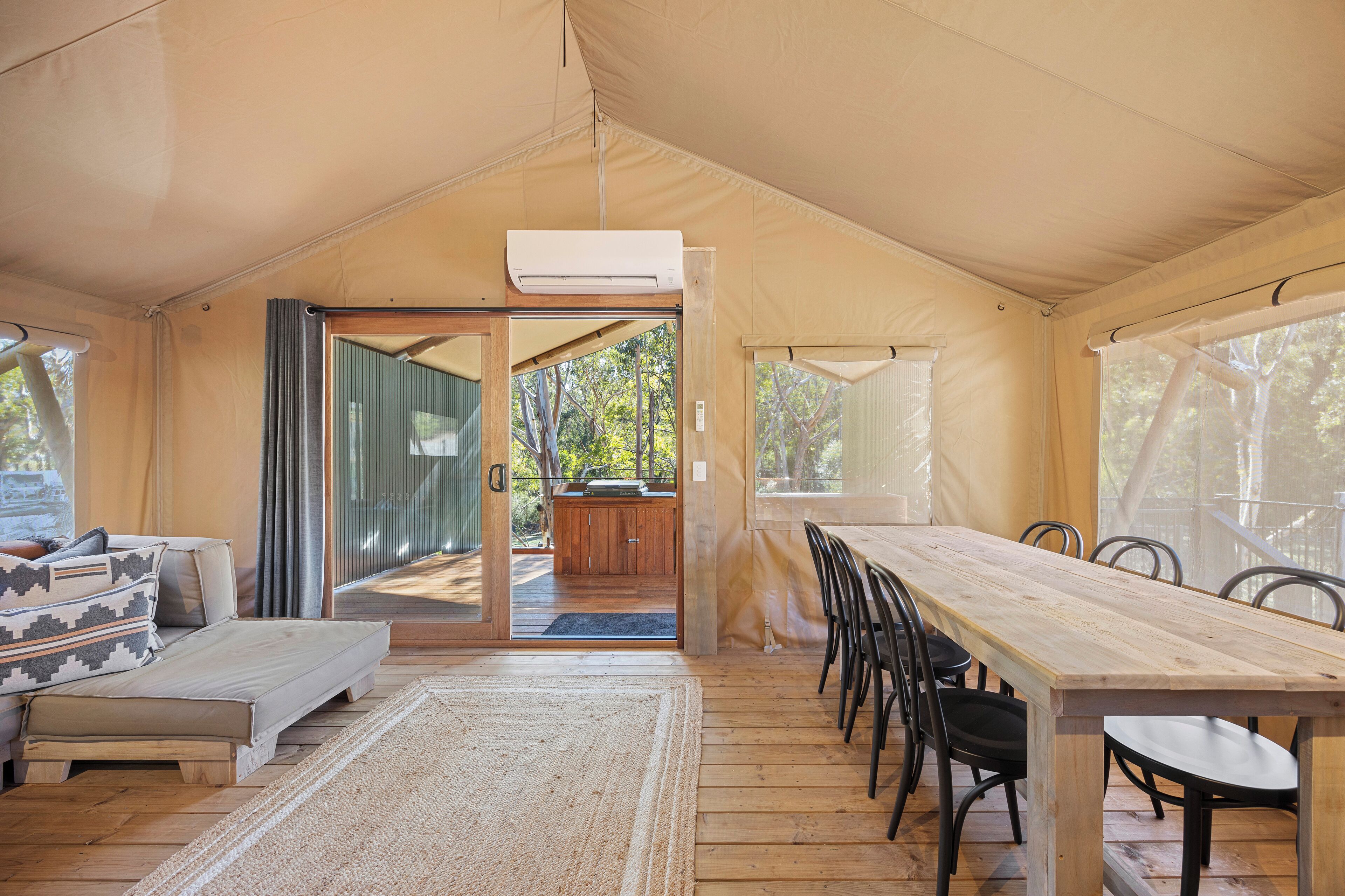 A tented accommodation with a dining area, a sofa, and a view of the outdoors.