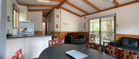 A cozy interior with a round table, chairs, a sofa, and a kitchen area with a counter and appliances.