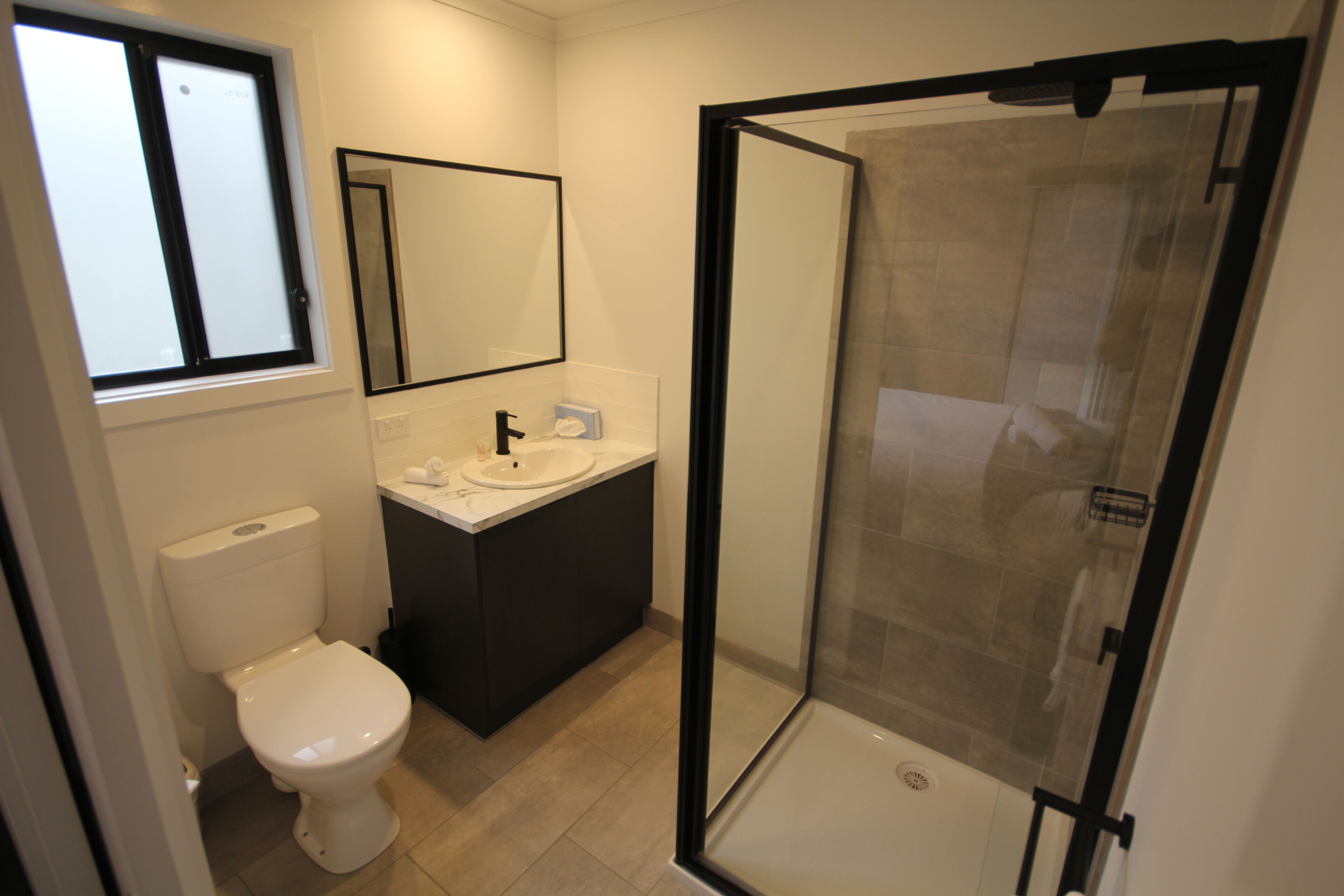 A modern bathroom with a toilet, sink, mirror, and glass-enclosed shower.
