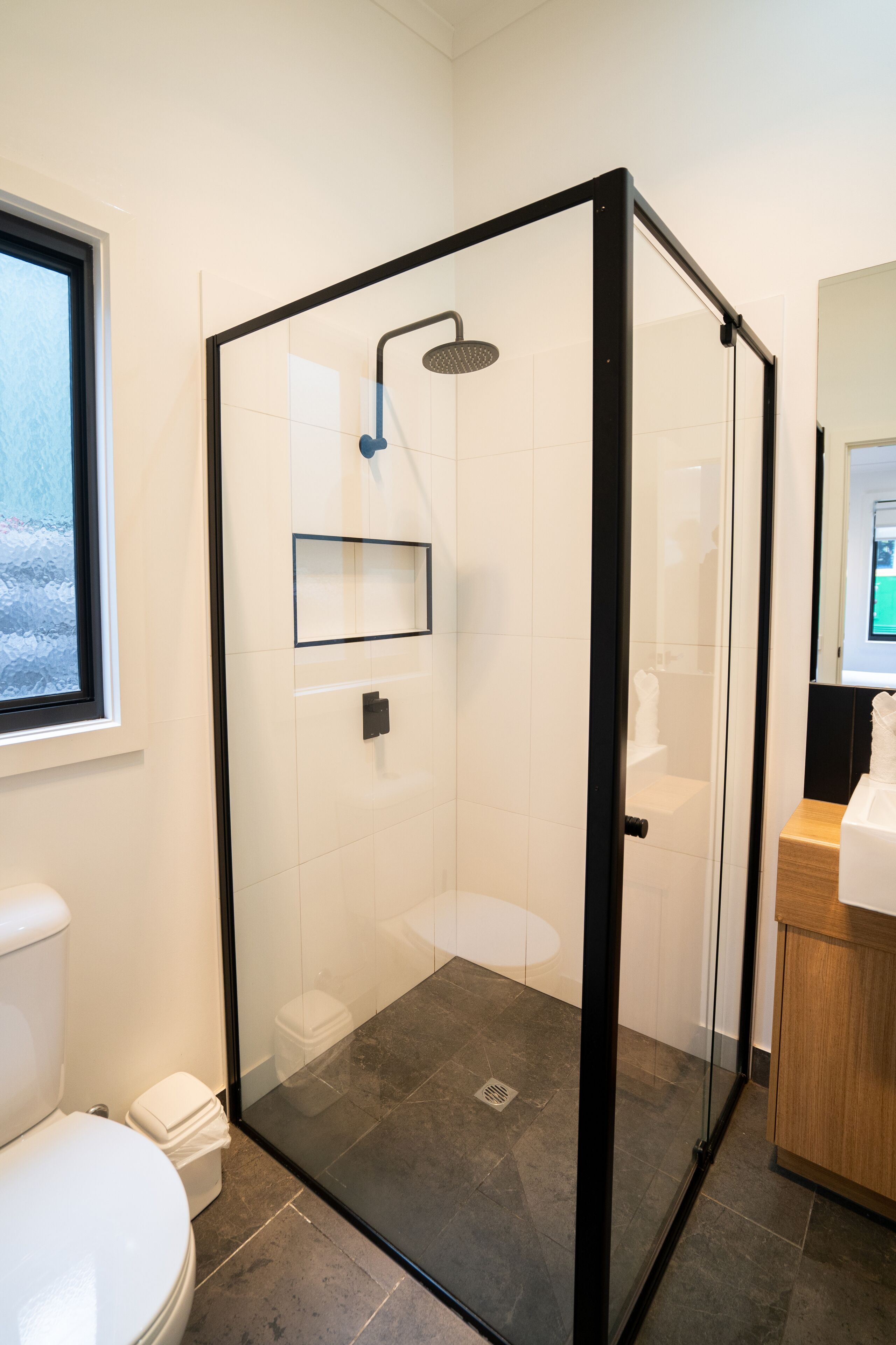 Une salle de bain moderne dotée d’une douche à parois de verre, de toilettes et d’un espace lavabo.