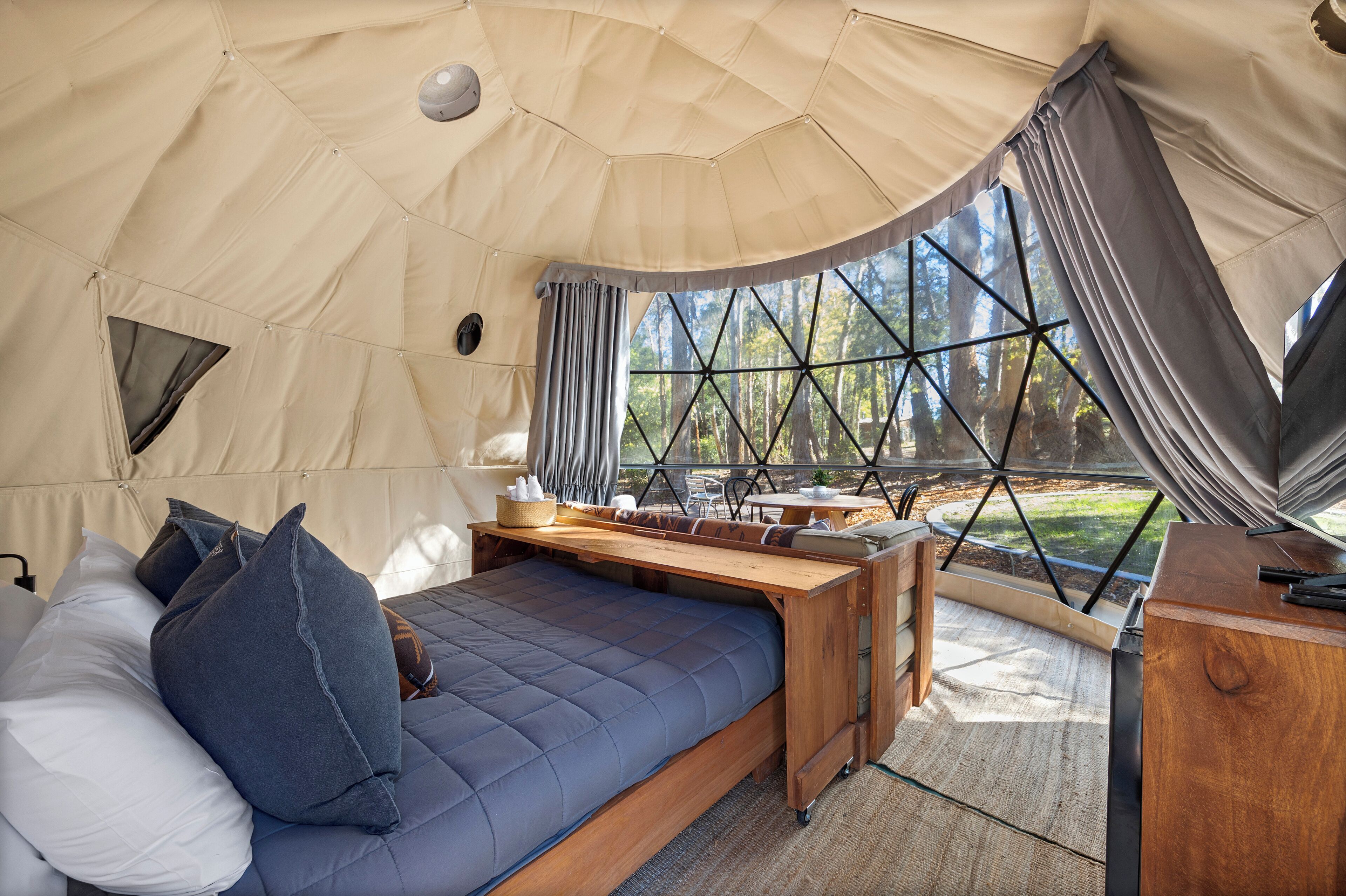 A tented accommodation with a bed, a desk, and a view of the outdoors.
