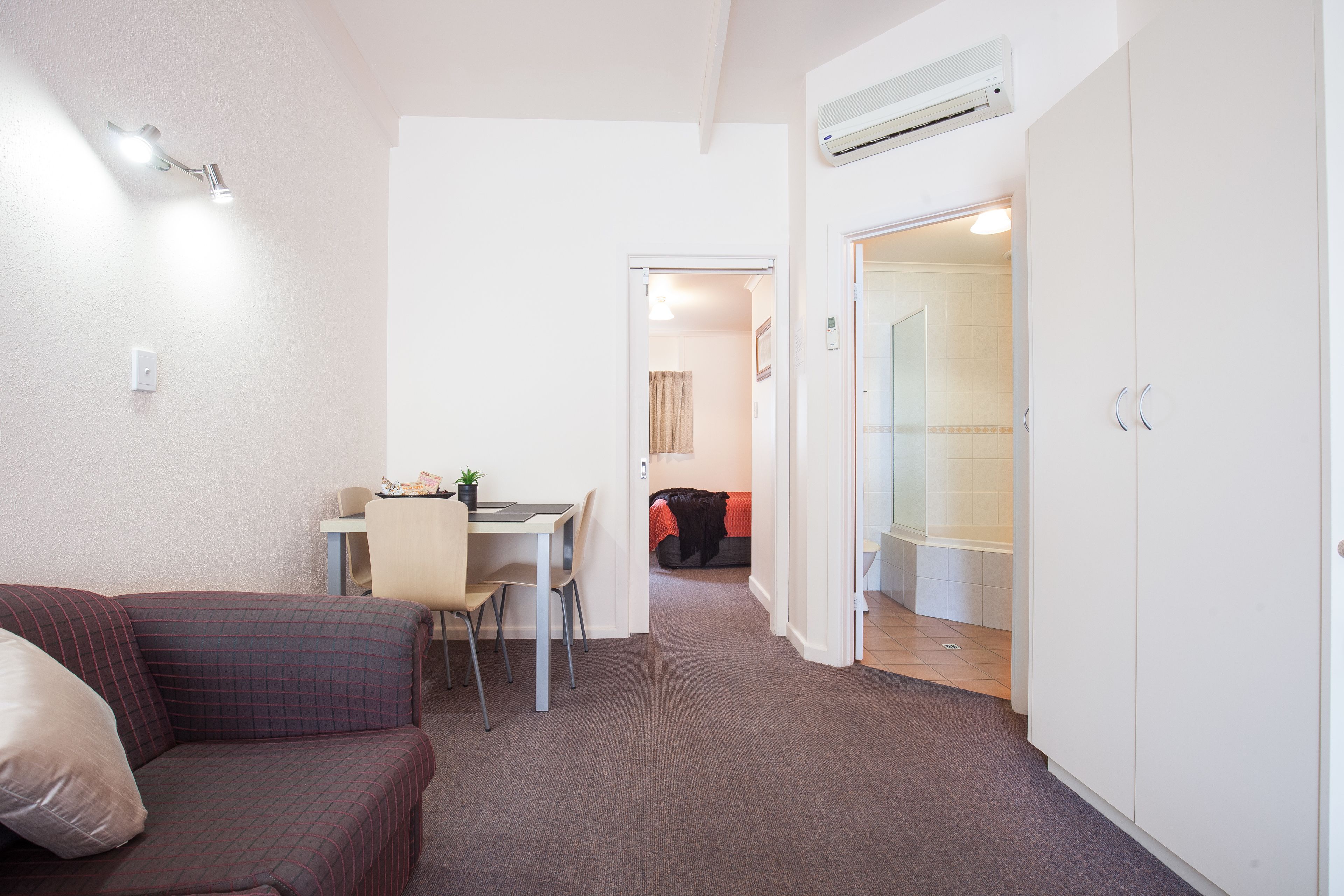 A compact living space with a sofa, a dining table with chairs, a bed, and a bathroom with a shower and toilet.
