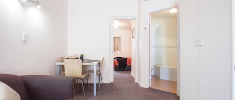 A compact living space with a sofa, a dining table with chairs, a bed, and a bathroom with a shower and toilet.
