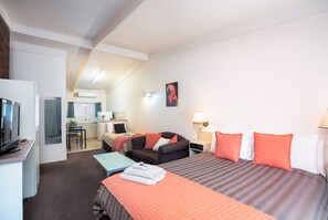 Una habitación de hotel con cama, escritorio, silla, televisión y kitchenette.