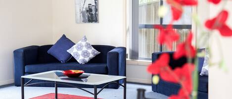 Una sala de estar moderna con un sofá azul, una mesa de centro de vidrio y un tapete rojo.
