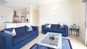 A living room with two sofas, a coffee table, and a kitchen in the background. - Mid City Motel - Mount Gambier (Mount Gambier)