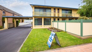 A two-story motel with a blue roof and beige exterior, featuring a signboard for all ground floor rooms. - Mid City Motel - Mount Gambier (Mount Gambier)