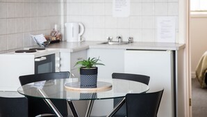 A modern kitchen with a round glass table, black chairs, a potted plant, and white cabinets. - Mid City Motel - Mount Gambier (Mount Gambier)