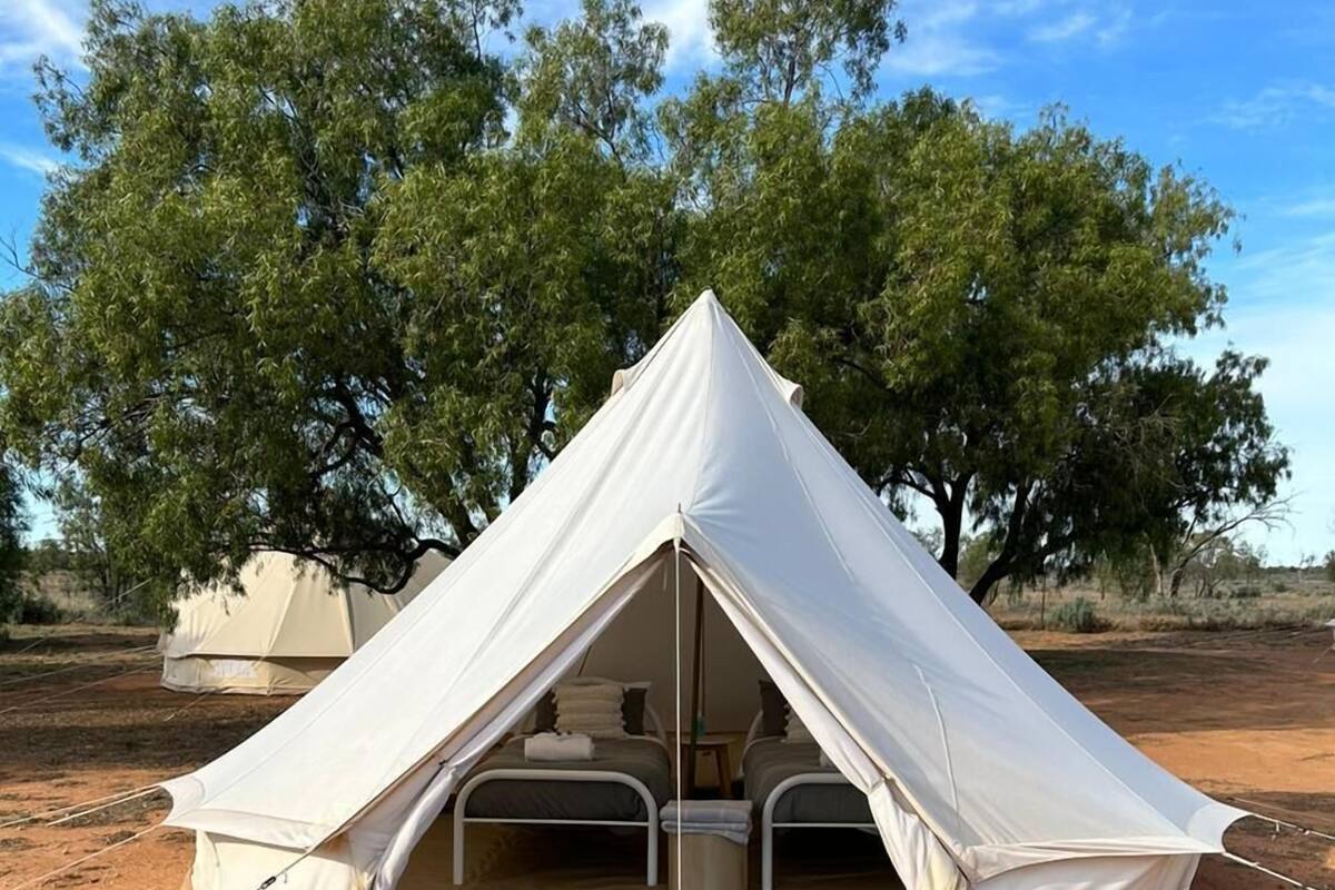 A dome-shaped tent with a wooden deck in front, set in a desert with sparse vegetation and trees in the background.
