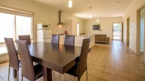A modern kitchen with a dining area, featuring a large table, chairs, a microwave, and a TV. - Mungo Lodge (Arumpo)