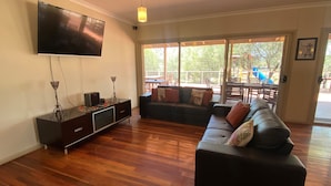 A living room with a flat-screen TV, a dark-colored sofa, and a wooden floor. - Mungo Lodge (Arumpo)