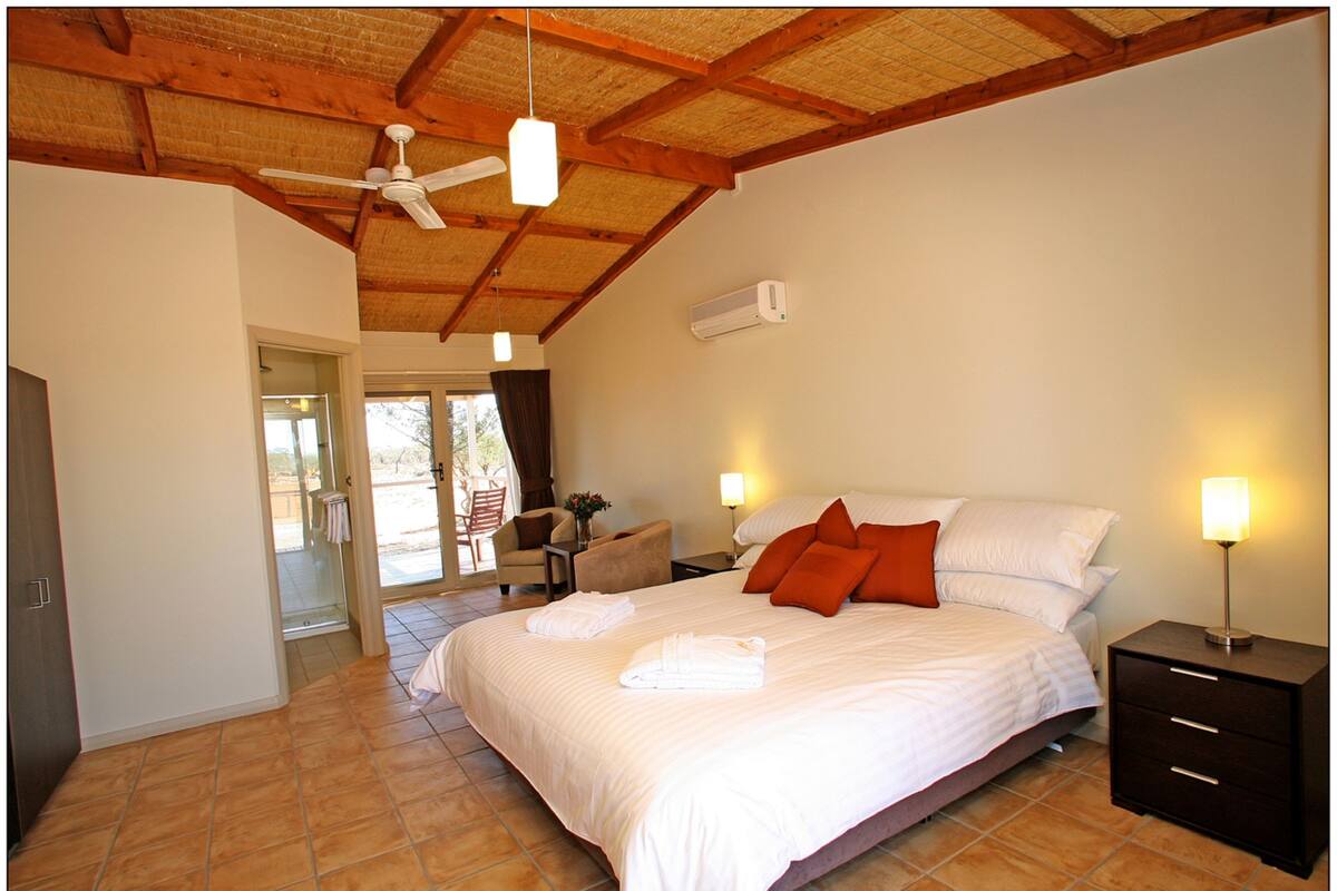 A bedroom with a bed, bedside lamps, a ceiling fan, and a window.