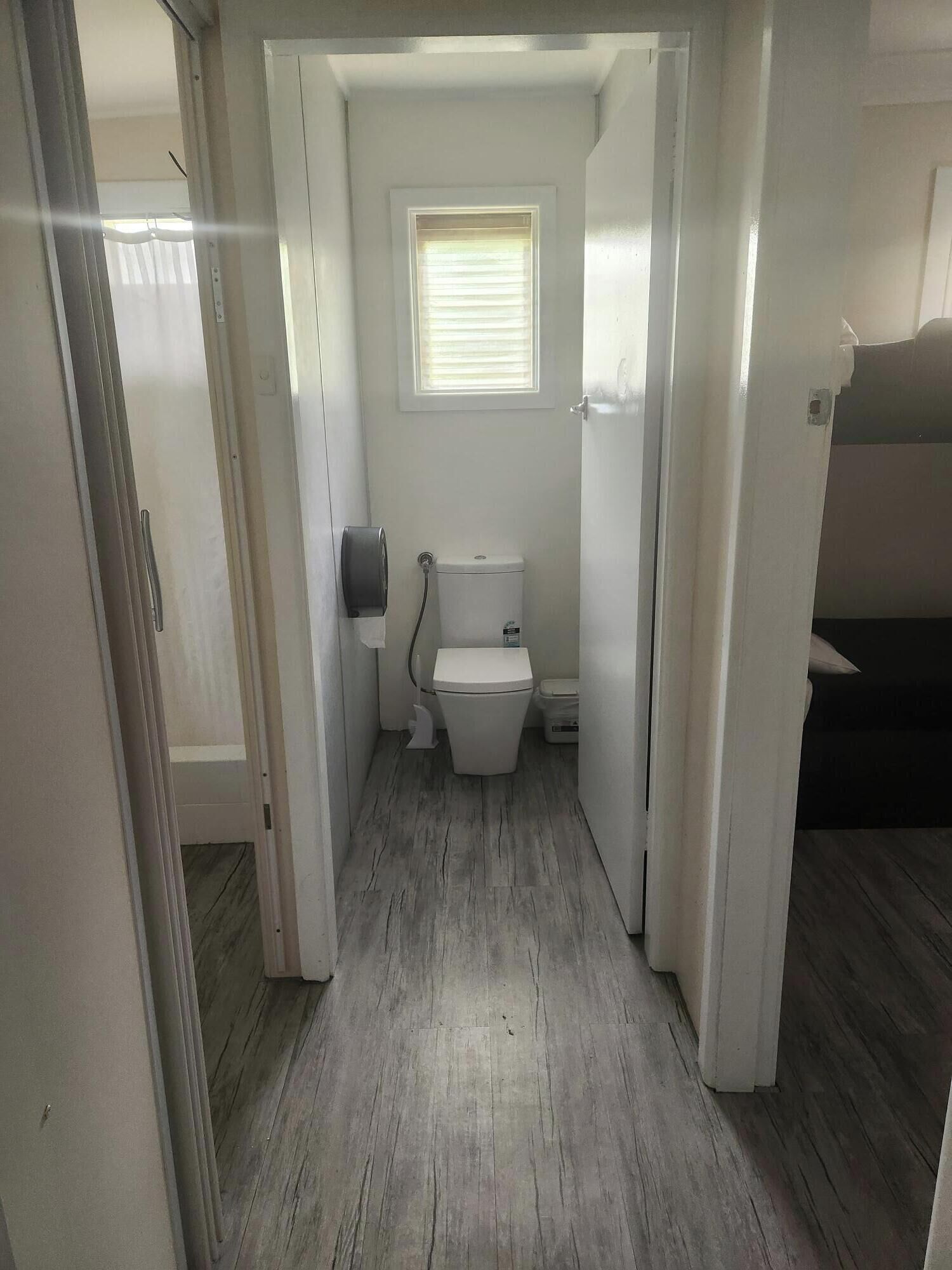 A narrow hallway leading to a small, white bathroom with a toilet and a window.