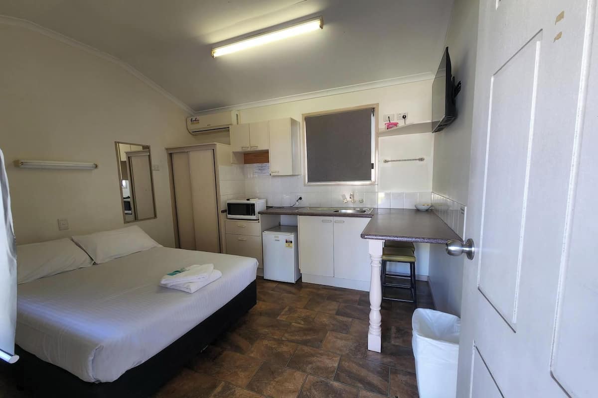 A compact room with a bed, a small kitchenette, and a bathroom.
