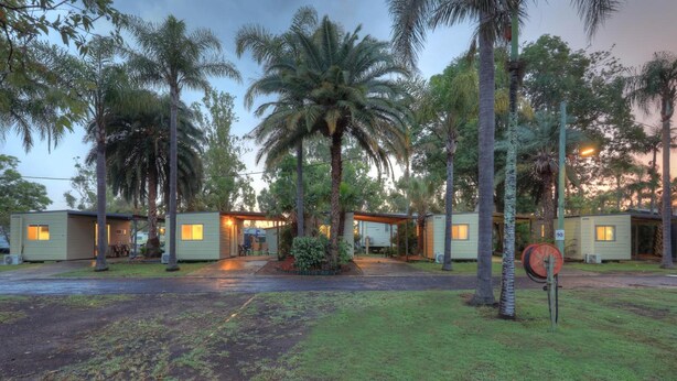A row of mobile homes with a central covered area, surrounded by palm trees and a grassy area. - Glenwood Tourist Park & Motel (South Grafton)