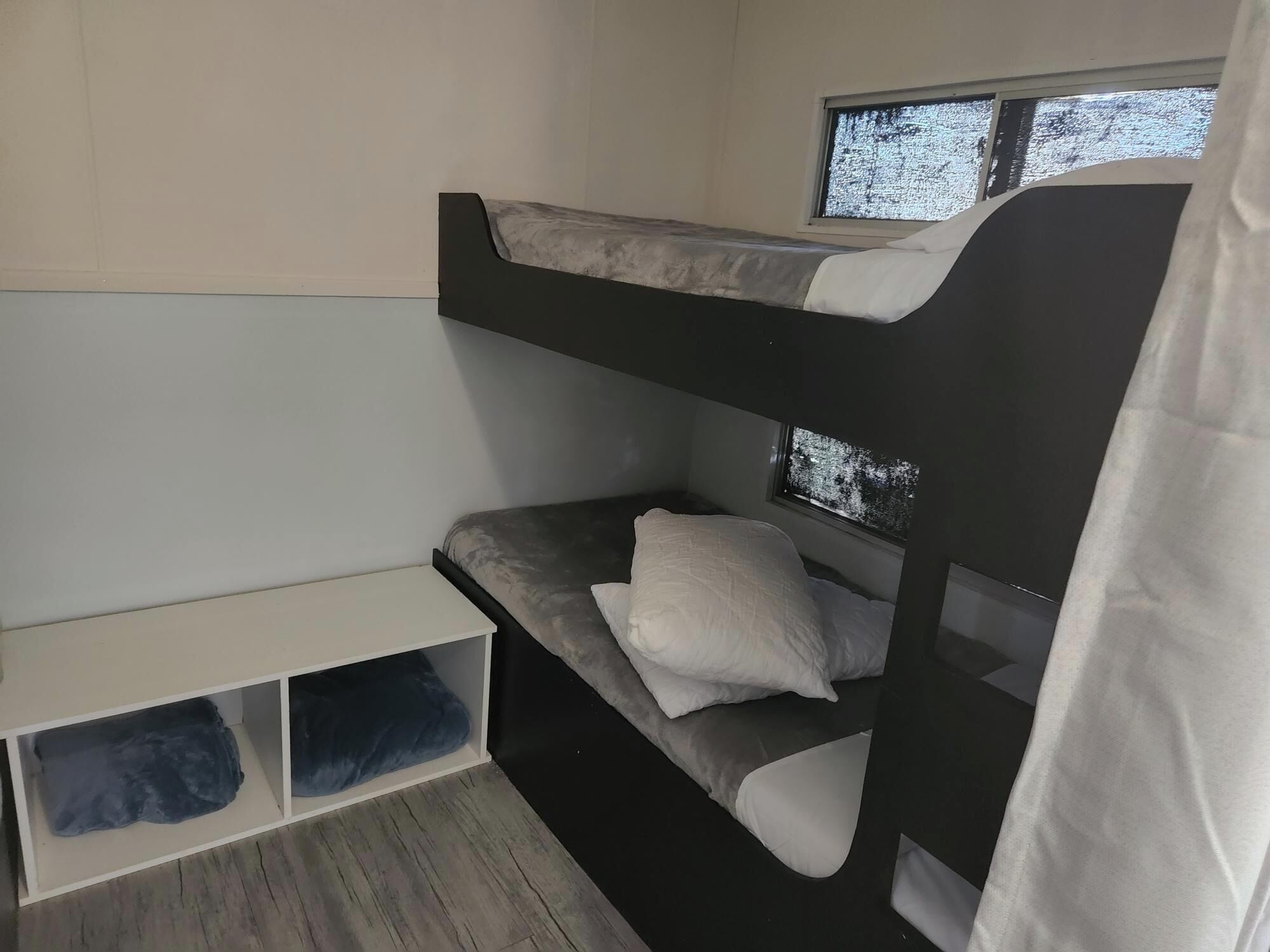 A bunk bed with a window, a white shelf below, and a curtain partially visible.