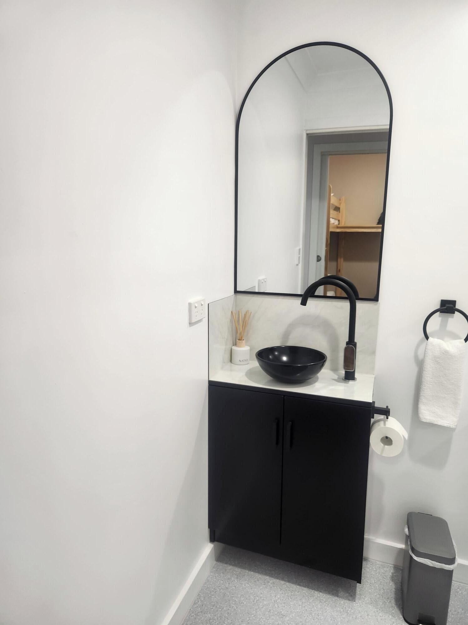 A modern bathroom with a black sink, a mirror, a towel, and a trash bin.
