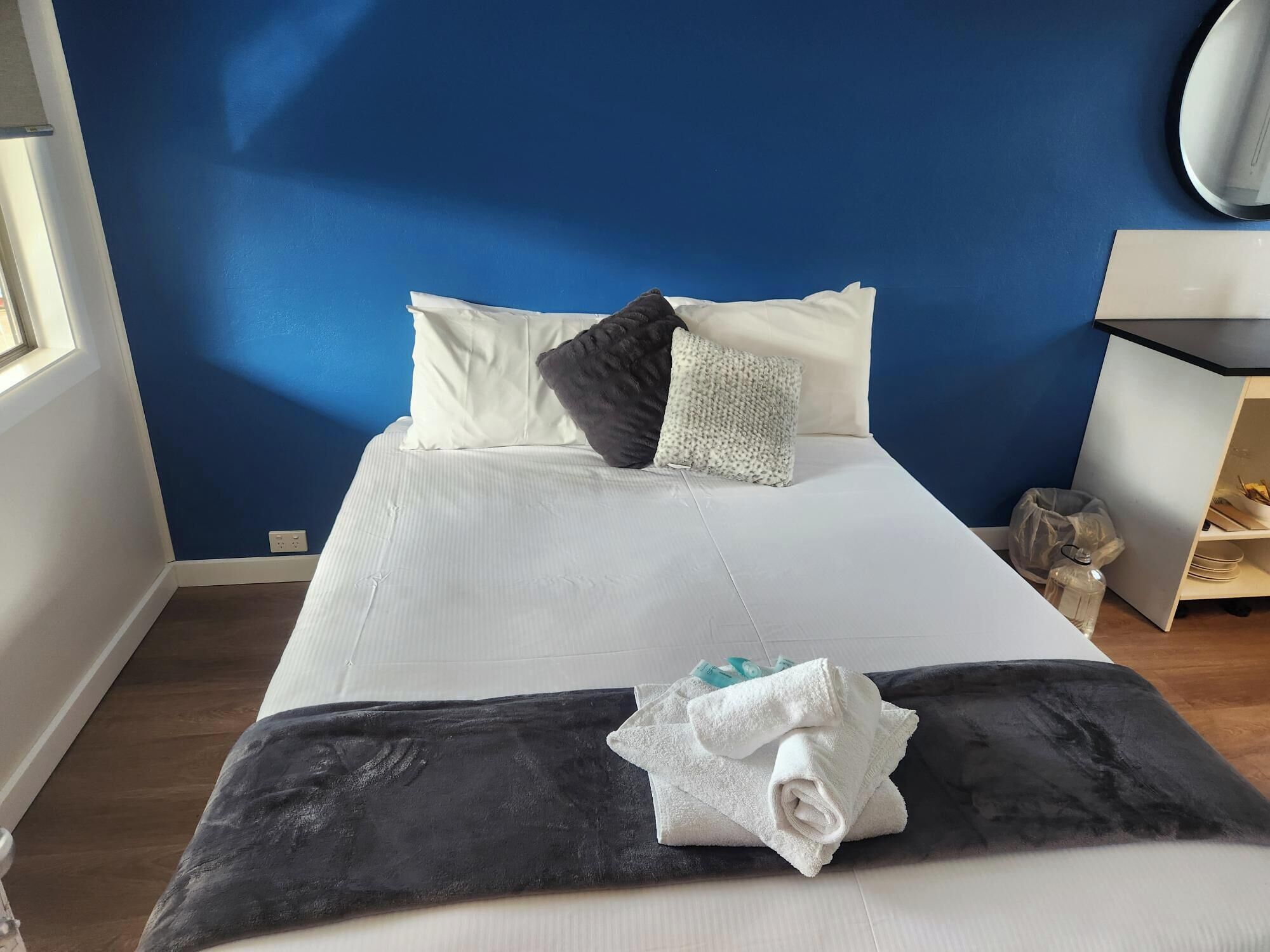 Una cama bien hecha con sábanas blancas y una manta negra, almohadas y una mesita de noche con una lámpara.