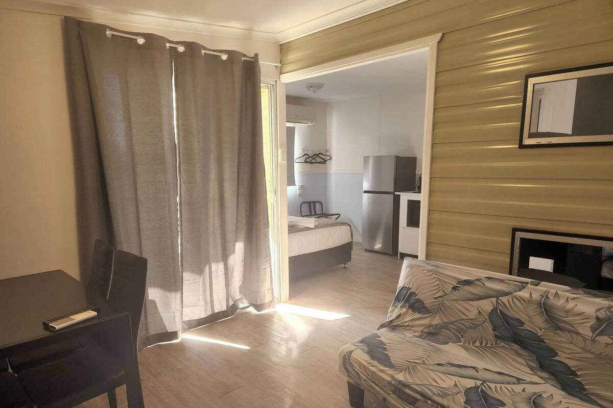 A compact living space with a bed, a sofa, a desk, and a kitchenette.