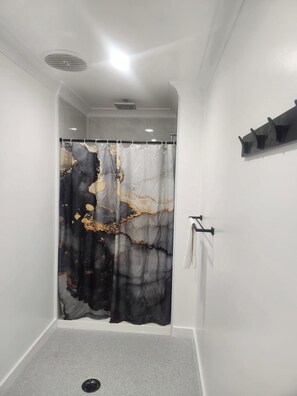 A bathroom with a shower curtain featuring a black and gold abstract design, a white towel rack, and a black shelf. - Glenwood Tourist Park & Motel (South Grafton)