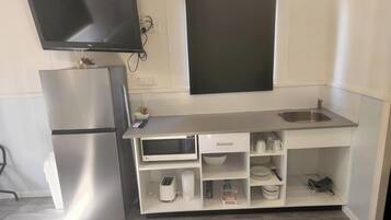 Une petite cuisine équipée comprenant un réfrigérateur en acier inoxydable, un four à micro-ondes, un évier et un téléviseur à écran plat fixé au-dessus du plan de travail.