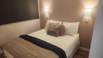 A neatly made bed with a textured blanket, two wall-mounted lights, and a dark headboard.