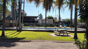Zona de piscina con mesa de picnic, rodeada de palmeras y una valla.