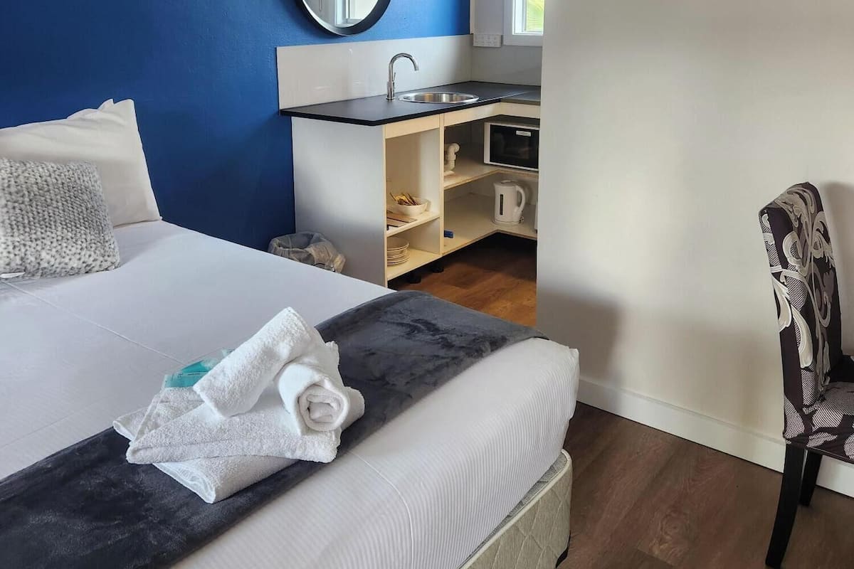 A hotel room with a bed, a desk with a sink, a chair, and a mirror on the wall.