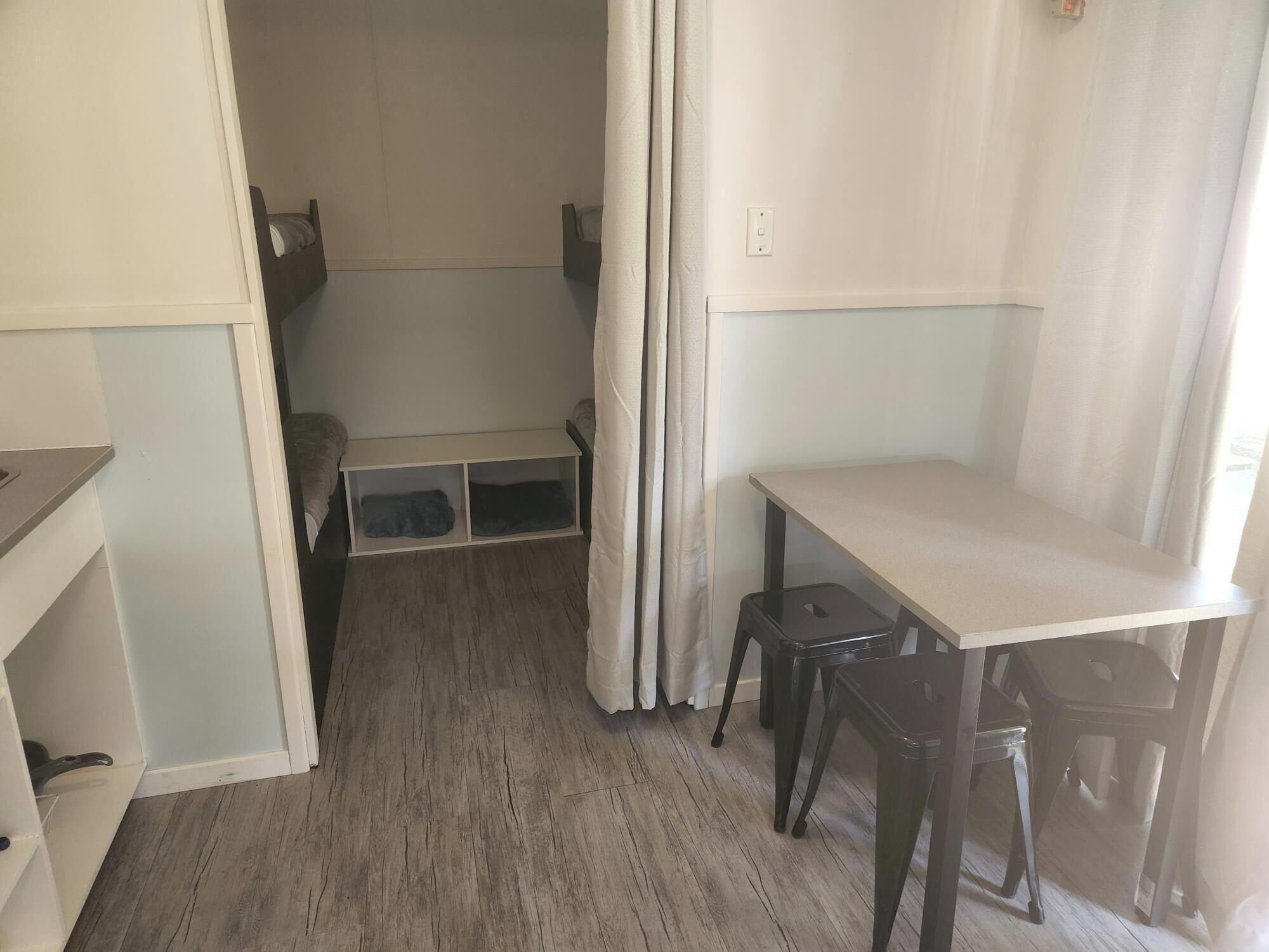 A small, compact room with a wooden floor, a single table, two chairs, and a built-in shelf unit.