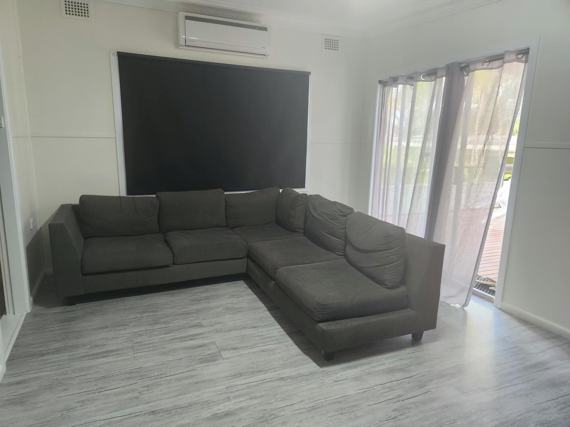 Una sala de estar moderna con un sofá seccional, un televisor de pantalla plana montado en la pared y un ventanal con cortinas translúcidas.