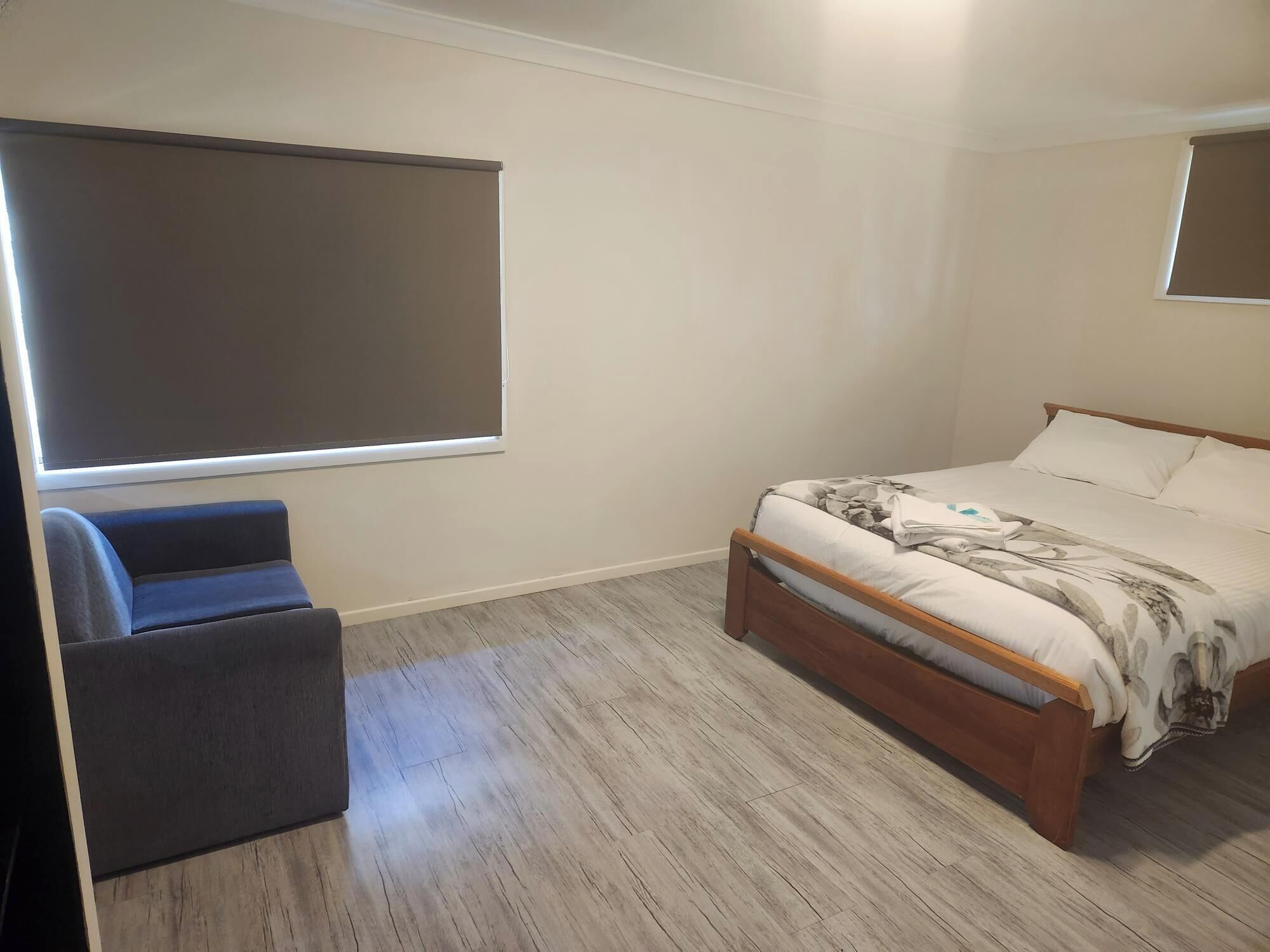 Quarto com cama, uma cadeira, uma janela grande e piso de madeira.