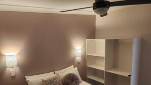 A bedroom with a bed, two wall-mounted lights, a ceiling fan, and a built-in shelving unit. - Glenwood Tourist Park & Motel (South Grafton)