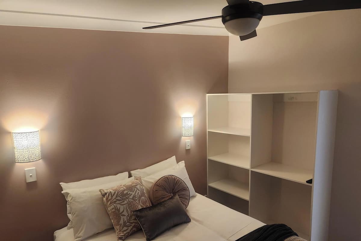 A bedroom with a bed, two wall-mounted lights, a ceiling fan, and a built-in shelving unit.
