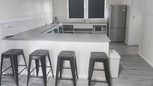 A modern kitchen with a central island, bar stools, a refrigerator, and a microwave. - Glenwood Tourist Park & Motel (South Grafton)