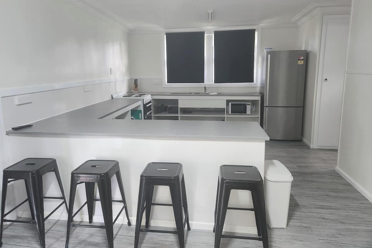 A modern kitchen with a central island, bar stools, a refrigerator, and a microwave.