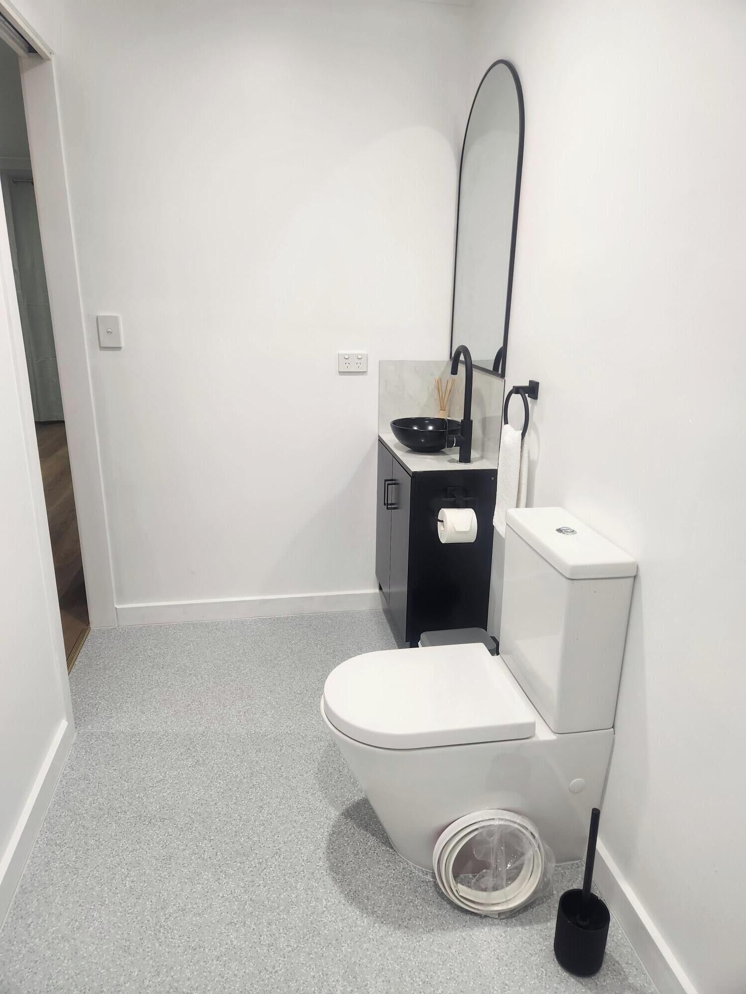 A small, modern bathroom with a white toilet, a black sink, and a mirror.