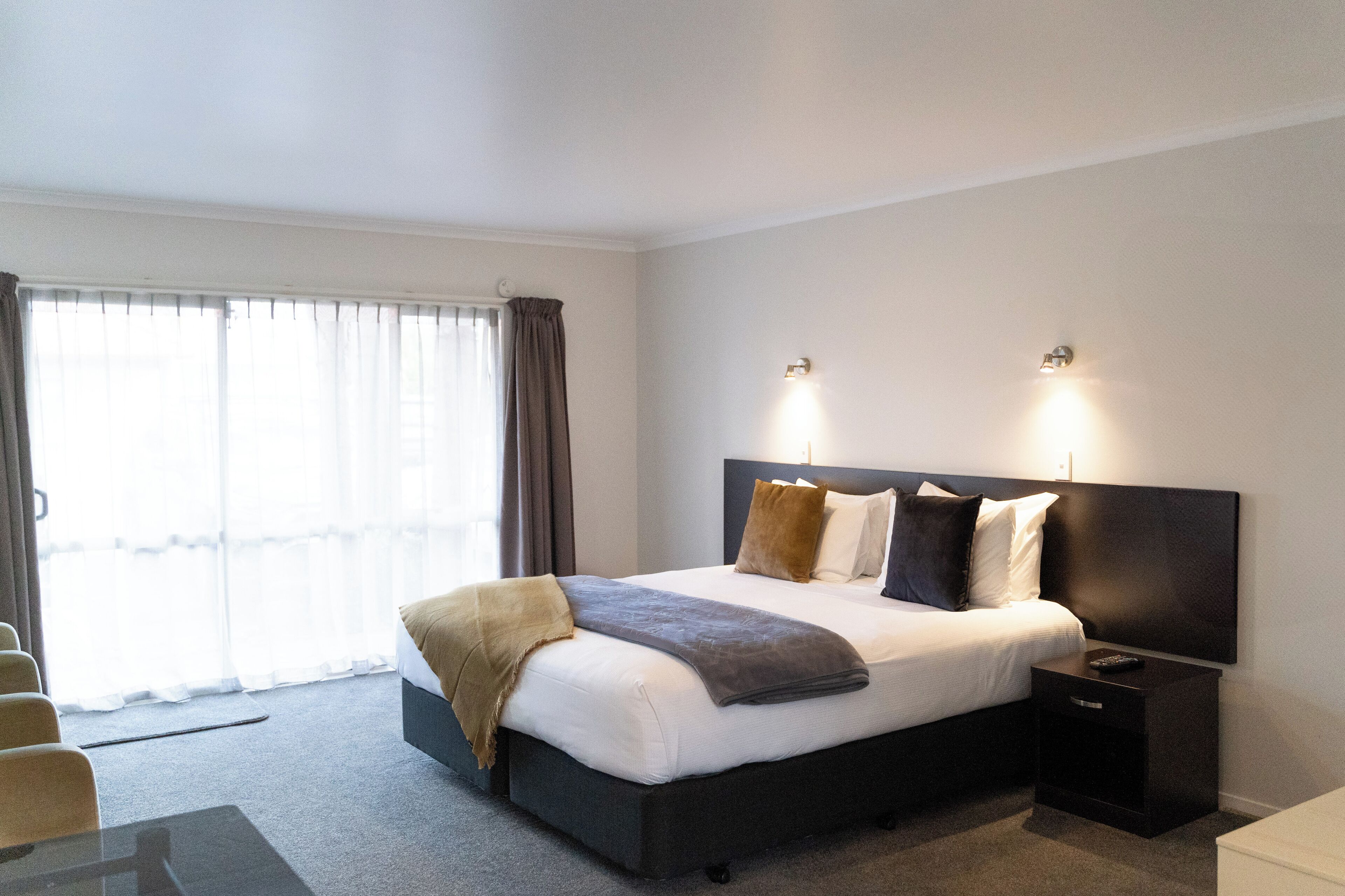A hotel room with a large bed, bedside tables, a desk, and a window with curtains.