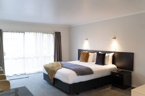 A hotel room with a large bed, bedside tables, a desk, and a window with curtains.