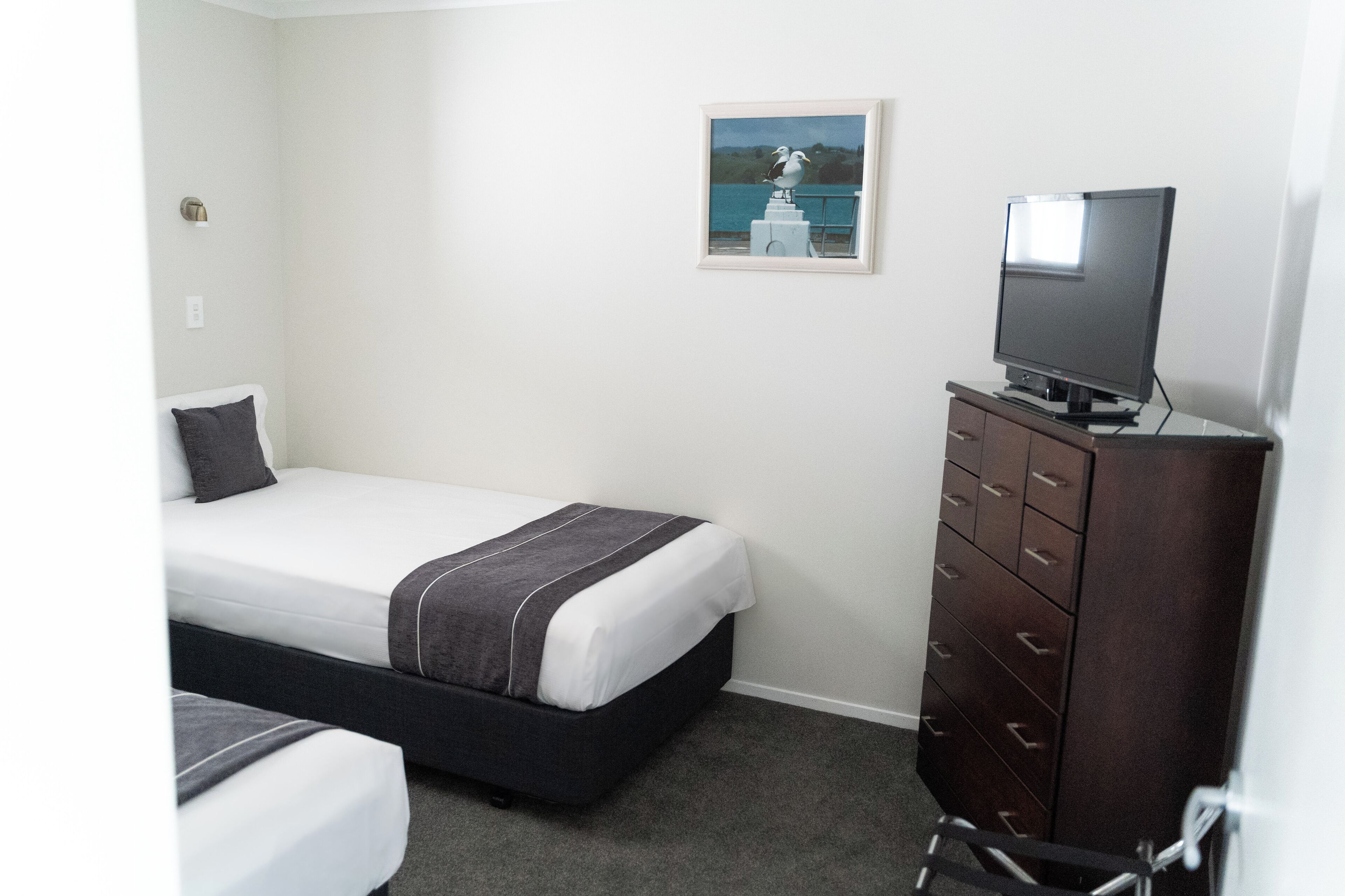 A hotel room with a single bed, a dresser, a television, and a framed picture on the wall.