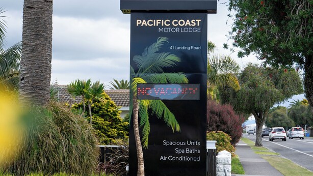 Señal del Pacific Coast Motor Lodge con temática tropical, que incluye palmeras y una playa.