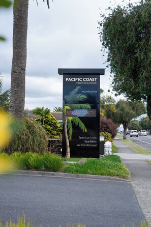 A sign for Pacific Coast Motor Lodge with a tropical theme, including palm trees and a beach scene. - Pacific Coast Motor Lodge (Whakatane)