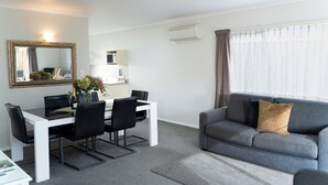 Una sala de estar moderna con comedor, sofá gris y un espejo grande.