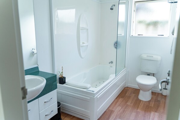 A modern bathroom with a bathtub, toilet, and a glass-enclosed shower. - Pacific Coast Motor Lodge (Whakatane)