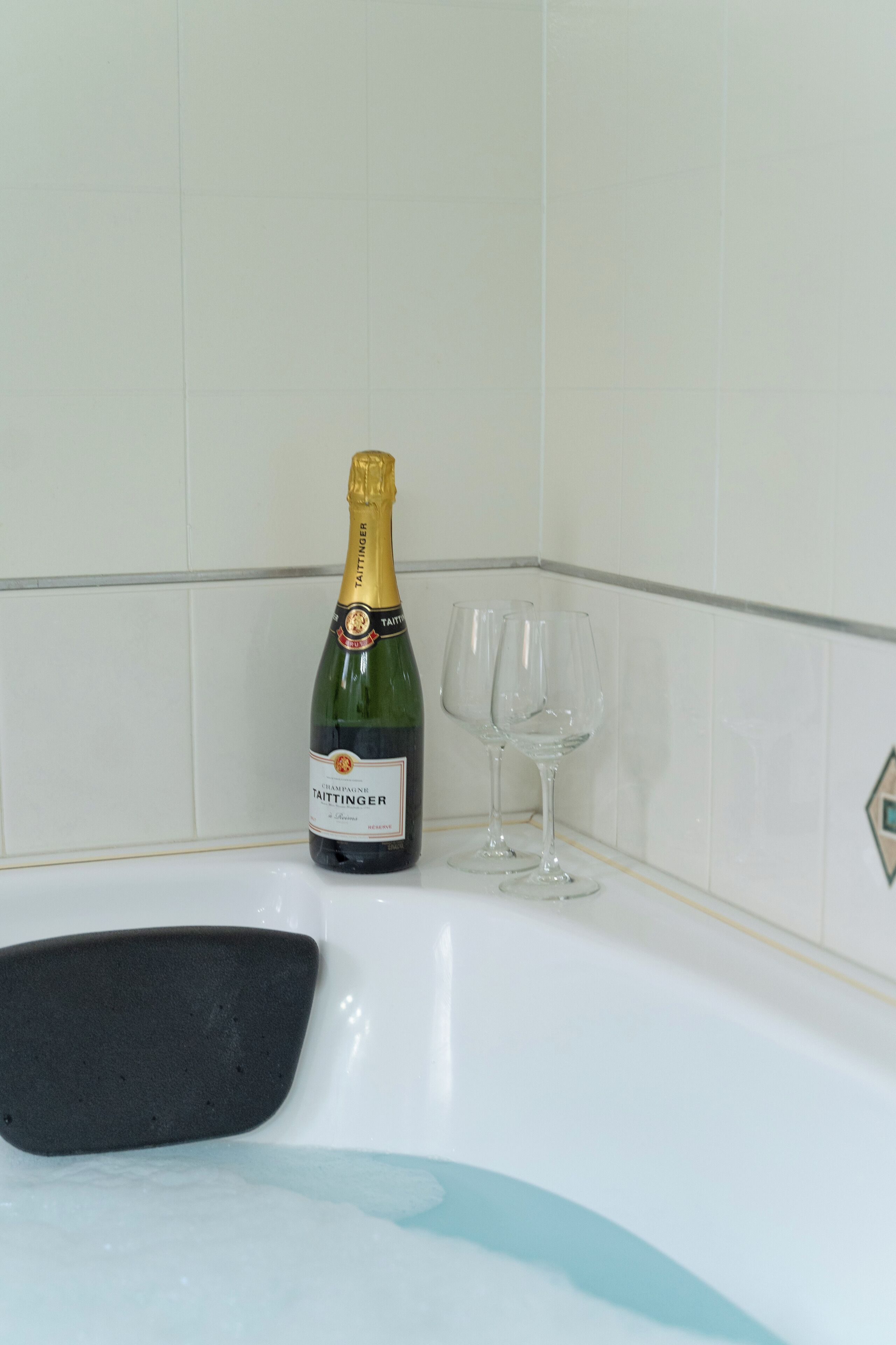 En flaske Taittinger champagne og to glas på et hvidt badekar.
