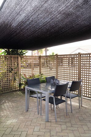 An outdoor patio with a table and chairs, a wooden fence, and potted plants.
