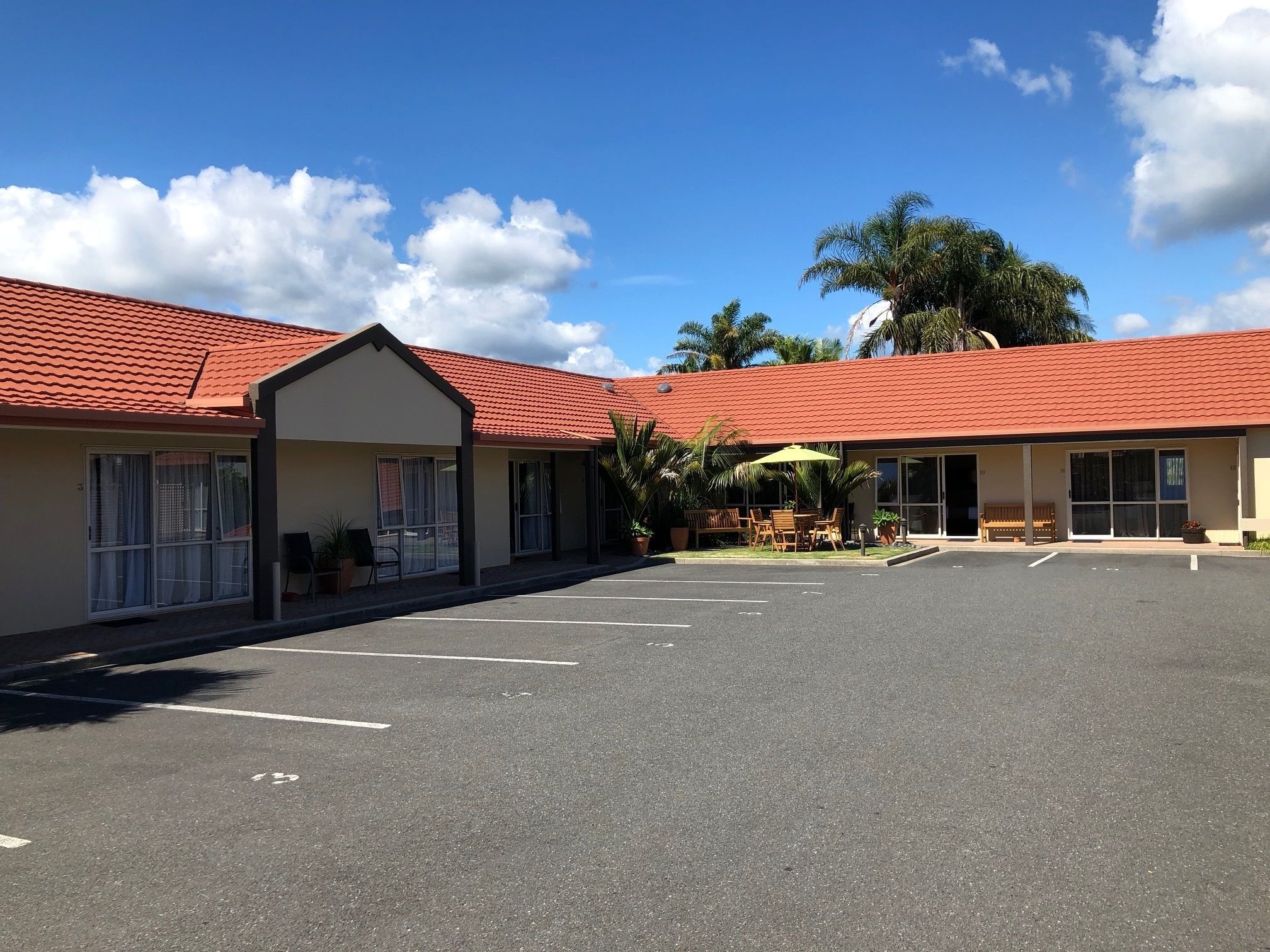 A motel with a red-tiled roof, a covered outdoor seating area, and a parking lot.